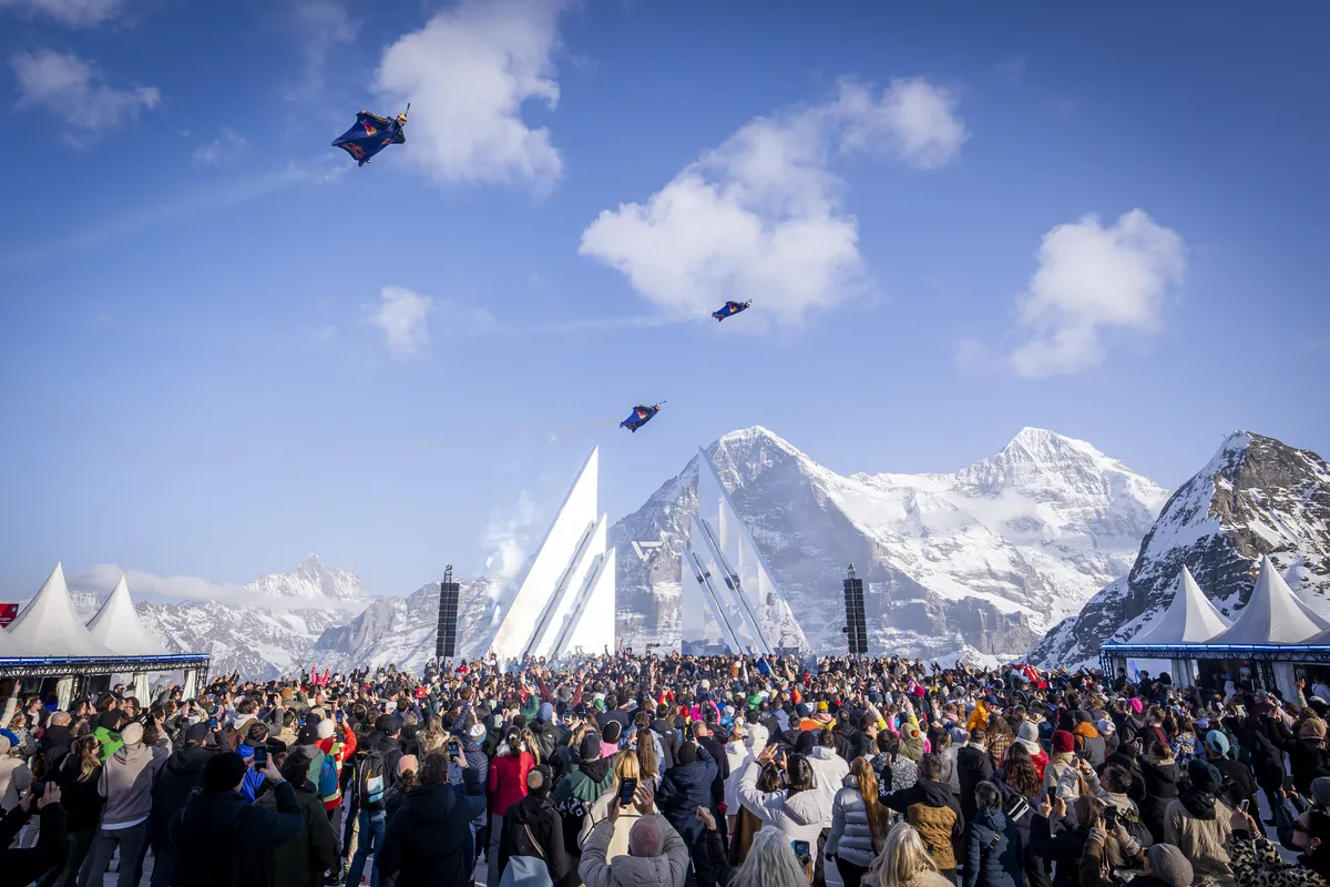 Zuschauermenge im Zielgelände blickt drei Wingsuit-Fliegern vor Eiger, Mönch und Jungfrau nach