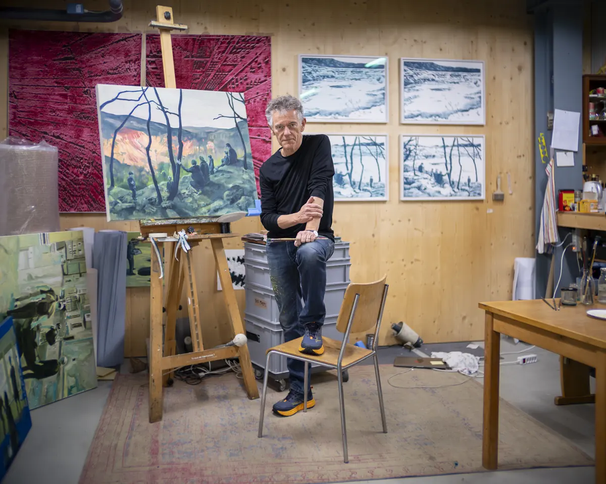 Maler in seinem Atelier, den Fuss auf einem Stuhl, umgeben von Gemälden und einer Staffelei