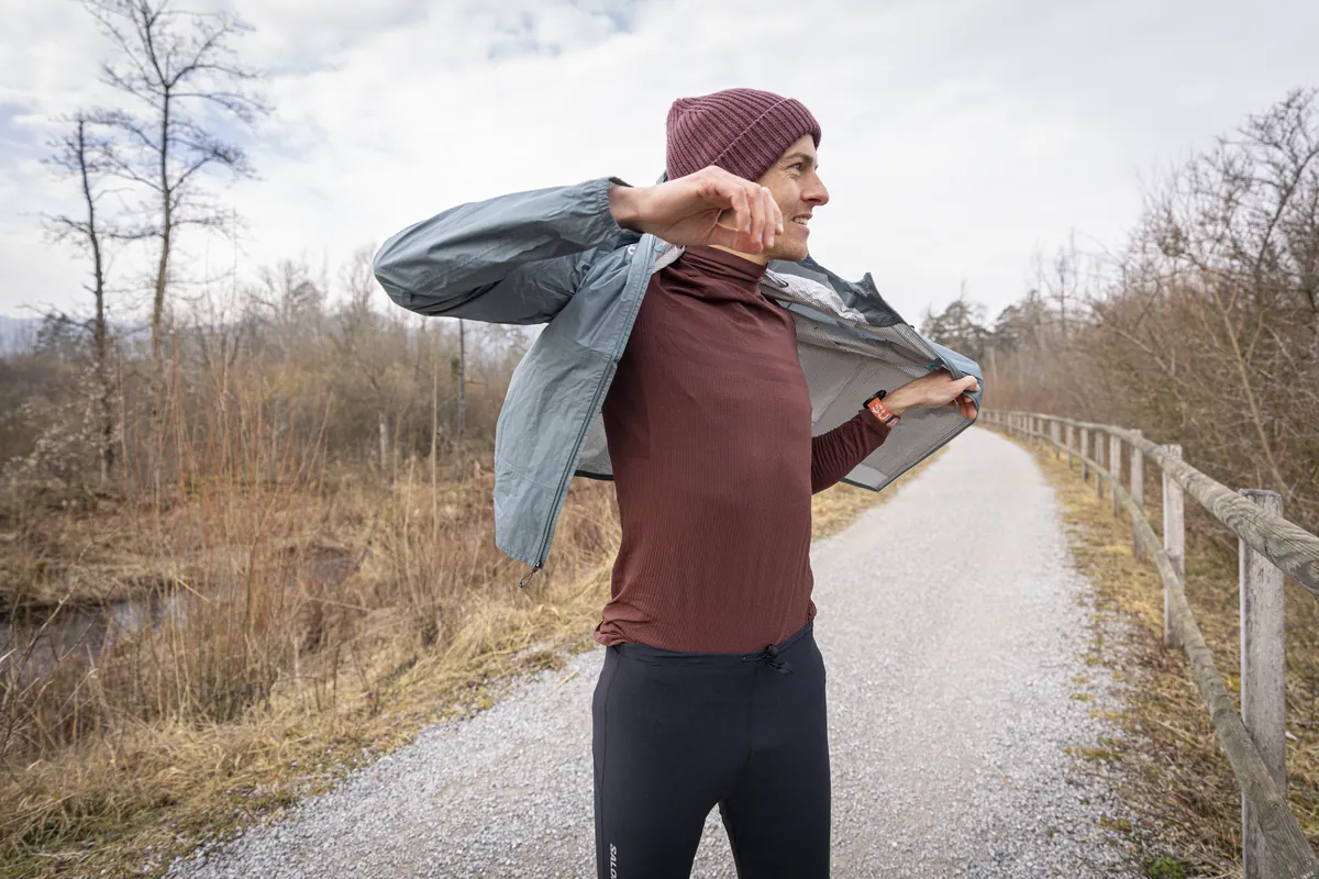 Läufer zieht auf einem Kiesweg entlang der Aue seine Windjacke über